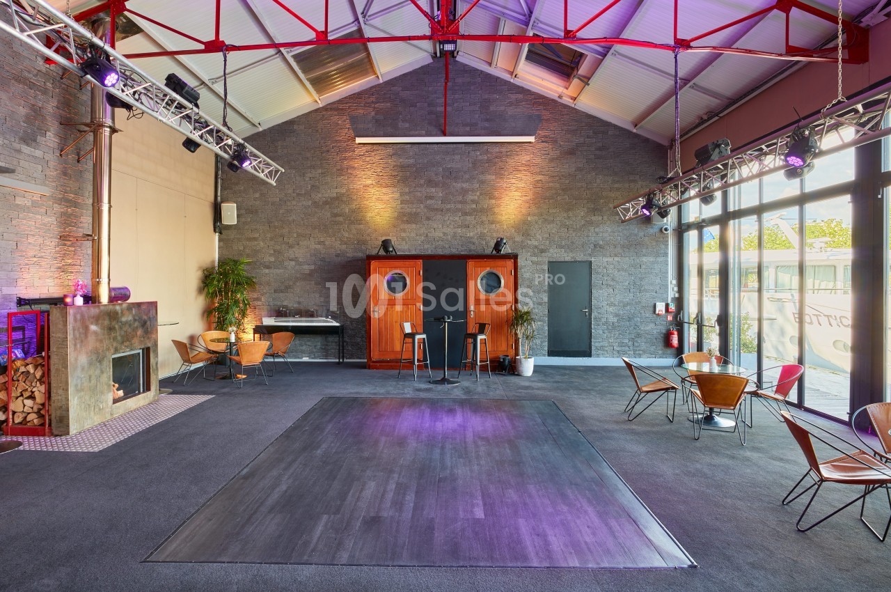Salle spacieuse avec parquet central, murs en pierre, mobilier moderne et éclairage coloré.