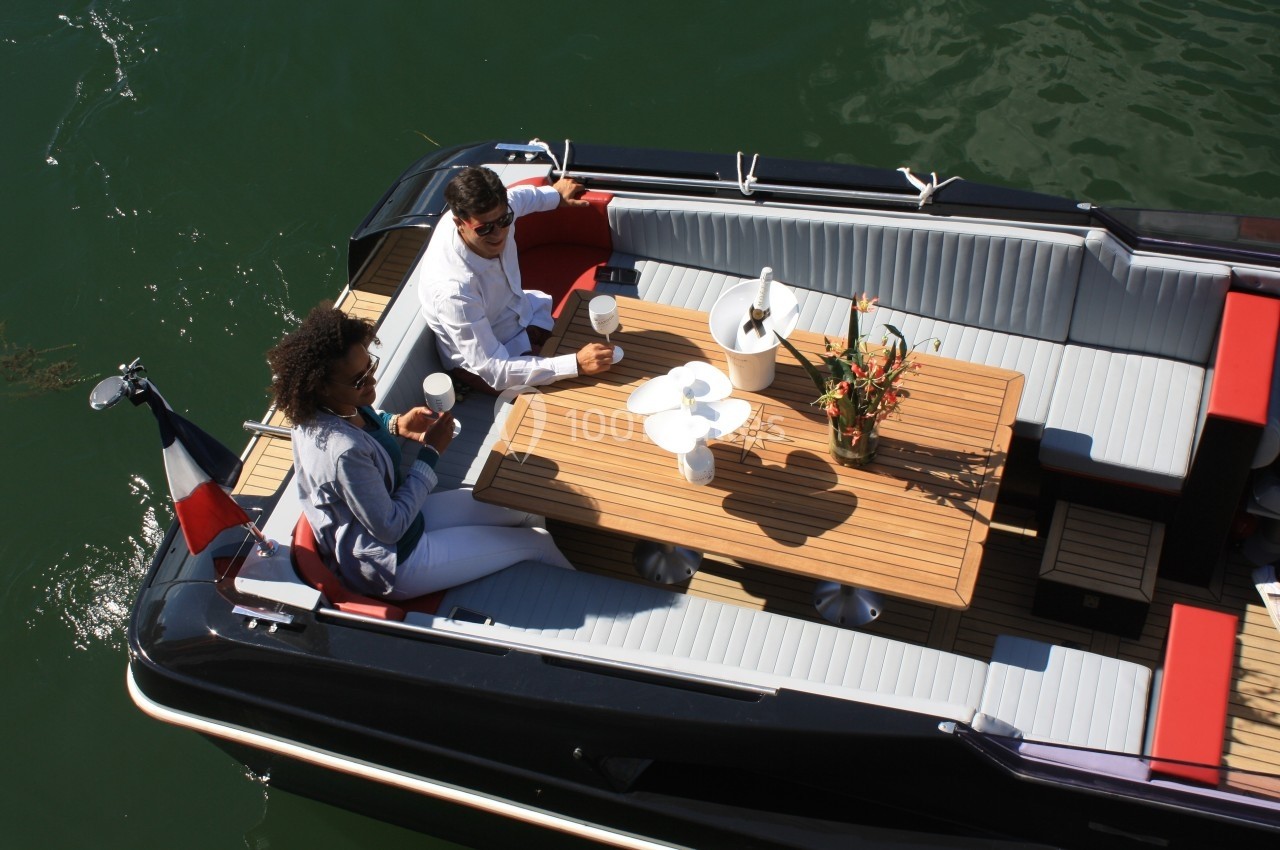 Deux personnes assises à bord d'un bateau, partageant une boisson autour d'une table en bois sur l'eau.