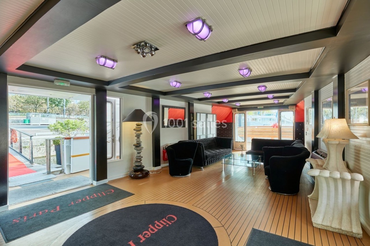 Intérieur lumineux d'un salon avec canapés noirs, lampes design et vue sur l'extérieur par des baies vitrées.