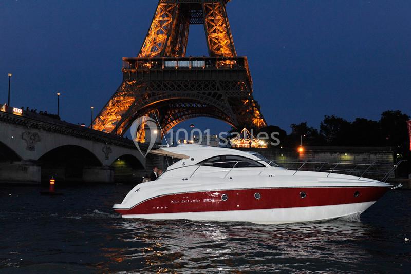 Un yacht blanc et rouge navigue sur la Seine, avec la tour Eiffel illuminée en arrière-plan.