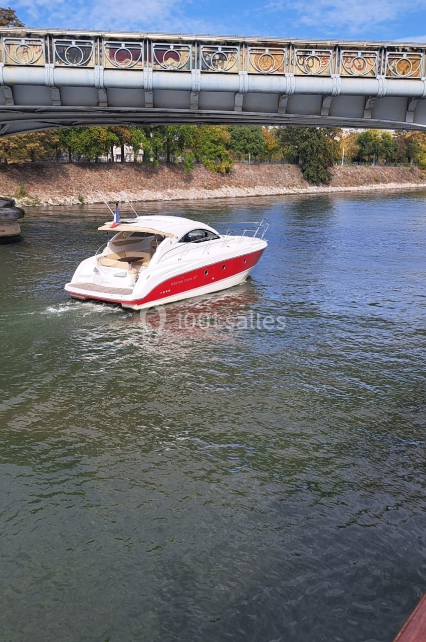 Bateau de plaisance rouge et blanc naviguant sur une rivière sous un pont décoré.