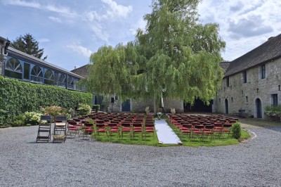 Cour intérieure d'un château avec pelouse, tables en bois, bâtiments en pierre et tours sous un ciel dégagé.