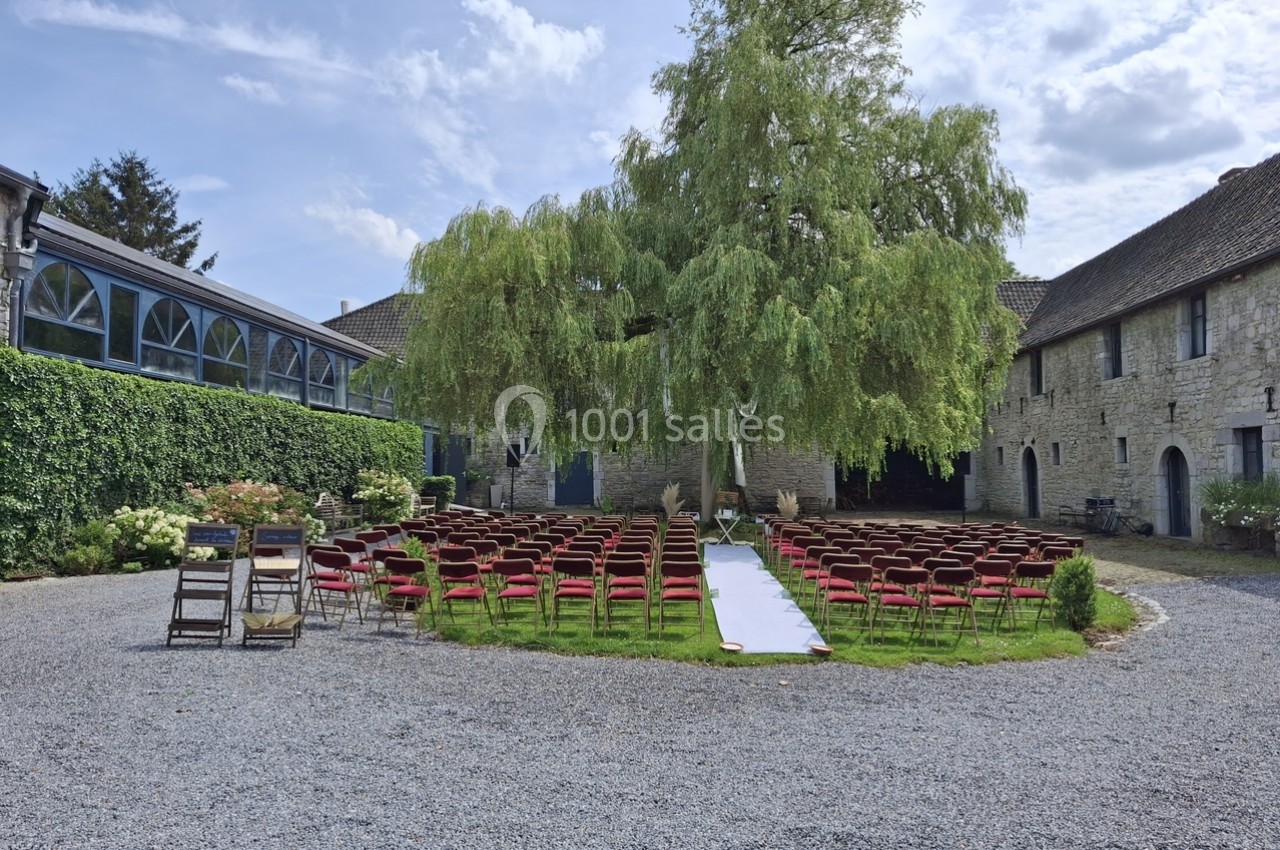 Chaises rouges disposées en extérieur sous un grand arbre pour une cérémonie, entourées de bâtiments en pierre.