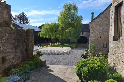 Cour intérieure d'un château avec pelouse, tables en bois, bâtiments en pierre et tours sous un ciel dégagé.