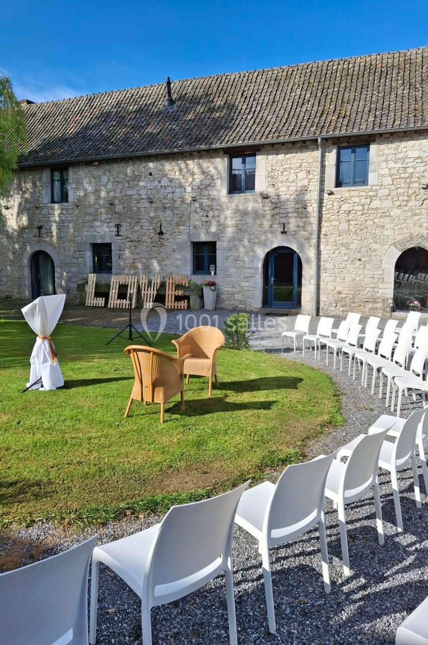 Chaises blanches disposées en cercle sur une pelouse devant une grange en pierre, avec le mot ’LOVE’ en décor.