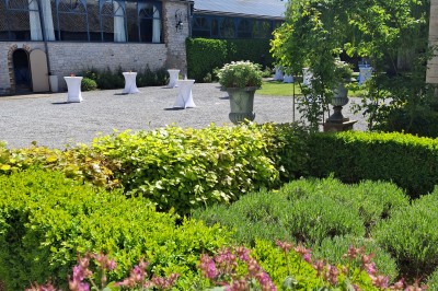 Cour intérieure d'un château avec pelouse, tables en bois, bâtiments en pierre et tours sous un ciel dégagé.