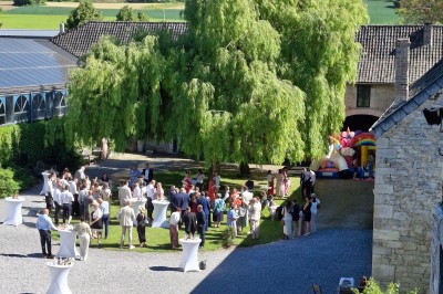 Cour intérieure d'un château avec pelouse, tables en bois, bâtiments en pierre et tours sous un ciel dégagé.
