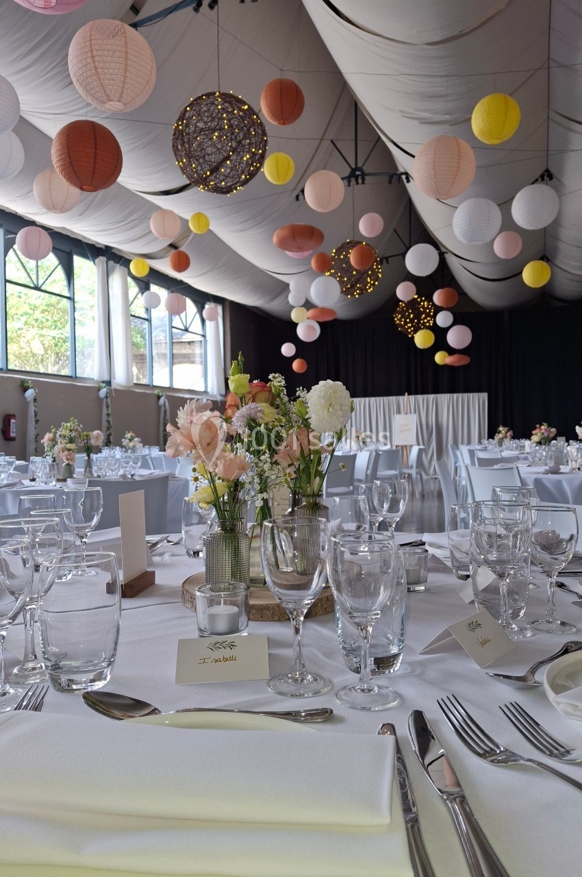 Salle de réception décorée avec des lanternes suspendues, tables dressées avec fleurs et vaisselle élégante.