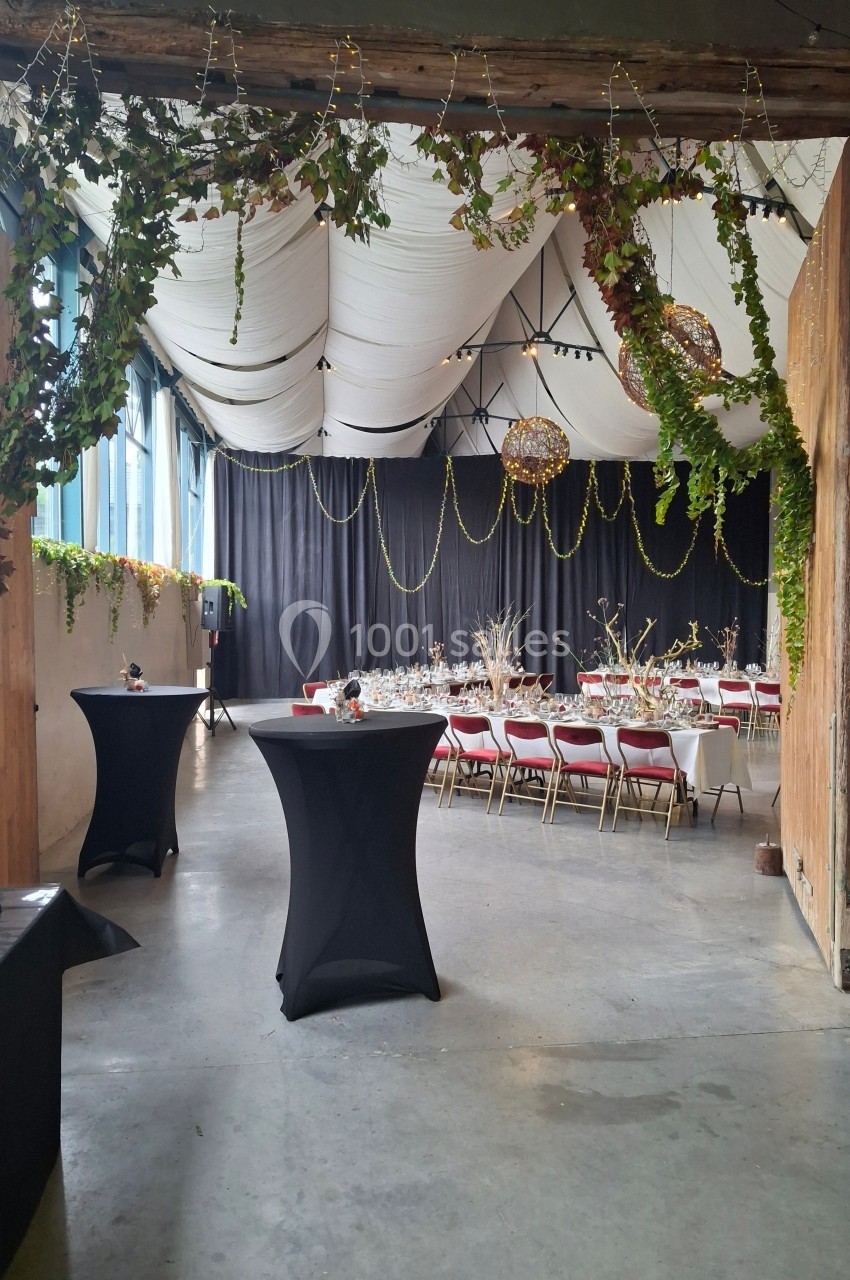 Salle de réception décorée avec des guirlandes lumineuses, des tables dressées et des chaises rouges.