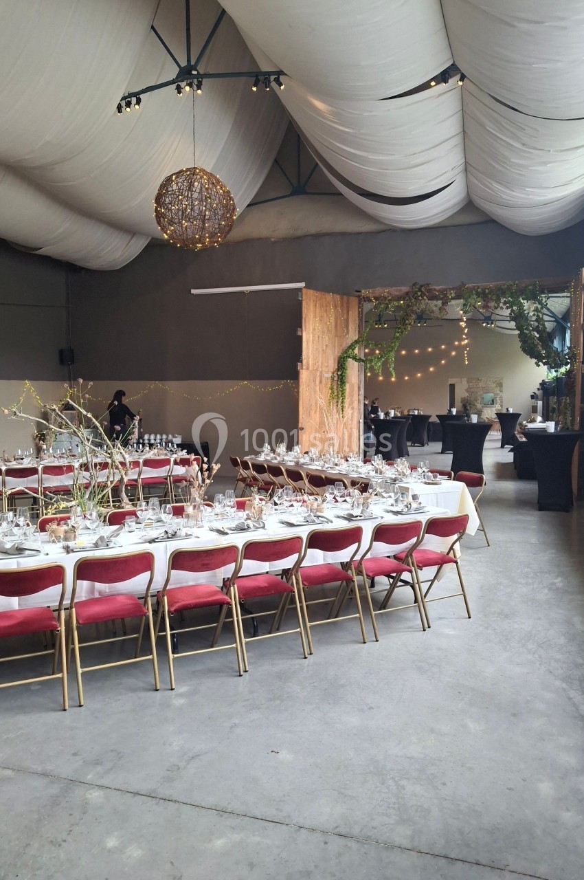 Salle de réception décorée avec des tables dressées, des chaises rouges, des guirlandes lumineuses et des éléments végétaux.