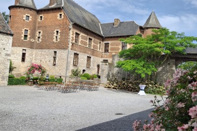 Cour intérieure d'un château avec pelouse, tables en bois, bâtiments en pierre et tours sous un ciel dégagé.