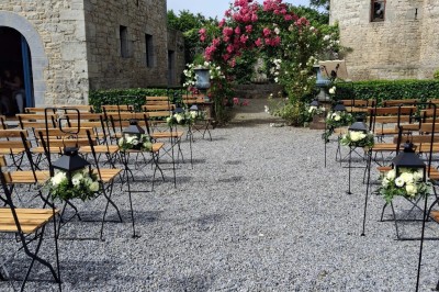 Cour intérieure d'un château avec pelouse, tables en bois, bâtiments en pierre et tours sous un ciel dégagé.