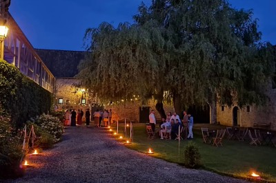 Cour intérieure d'un château avec pelouse, tables en bois, bâtiments en pierre et tours sous un ciel dégagé.