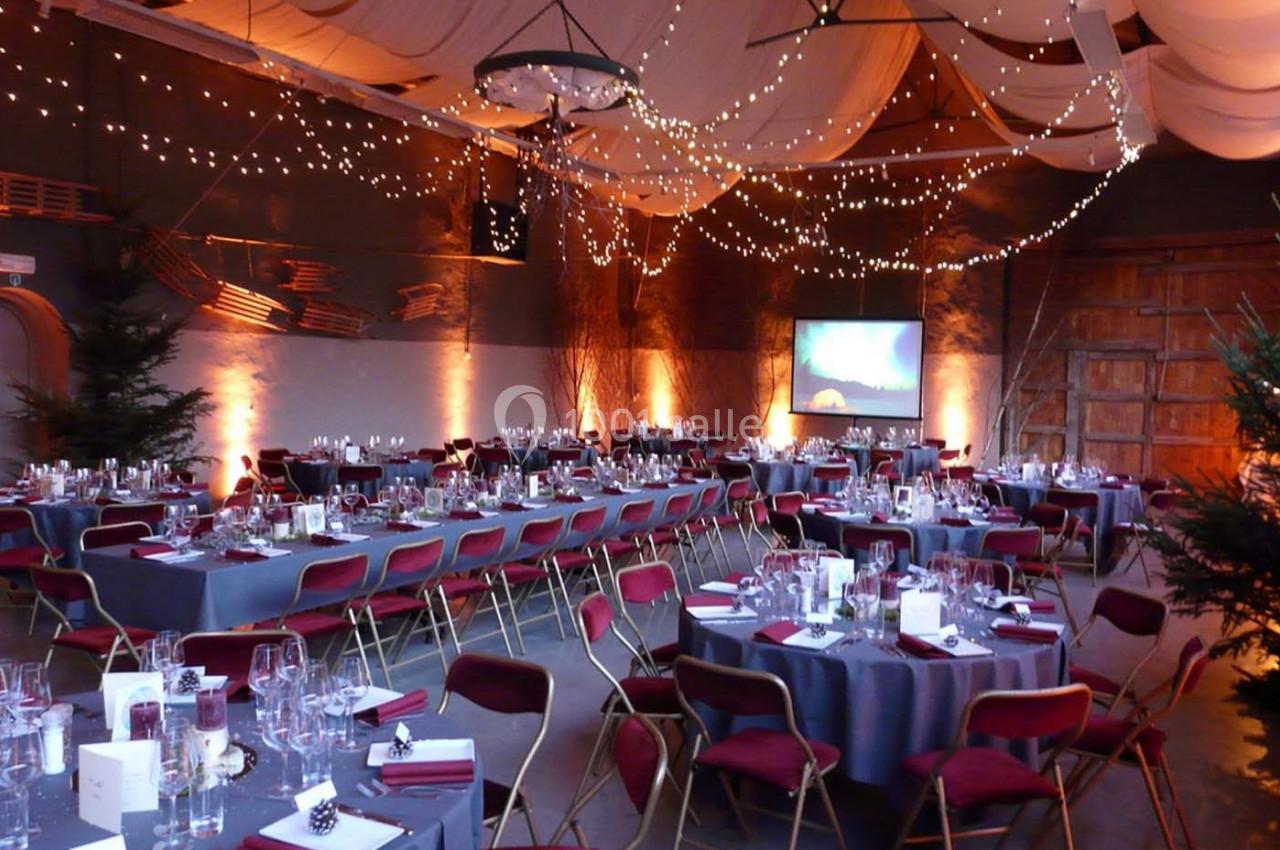 Salle de réception décorée avec des guirlandes lumineuses, des tables dressées et des chaises rouges.