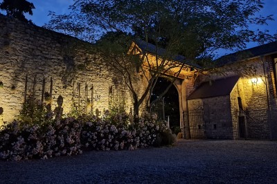 Cour intérieure d'un château avec pelouse, tables en bois, bâtiments en pierre et tours sous un ciel dégagé.