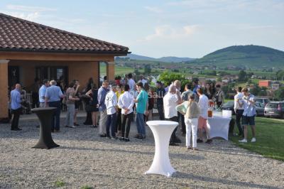 Bâtiment à un étage avec toit en tuiles, entouré de chemins, de pelouse et de vignes en arrière-plan.