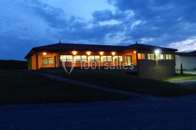 Bâtiment à un étage avec toit en tuiles, entouré de chemins, de pelouse et de vignes en arrière-plan.