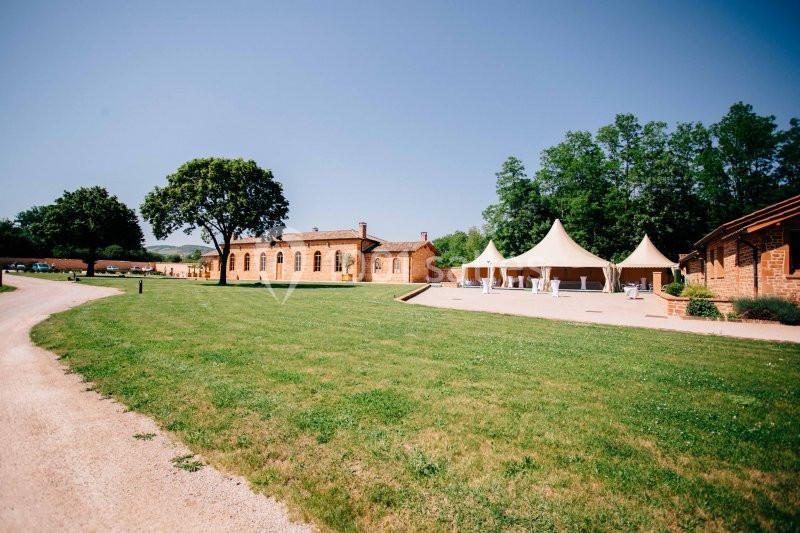 Bâtiments en briques rouges entourés de pelouses, avec des tentes blanches installées sur une terrasse ensoleillée.