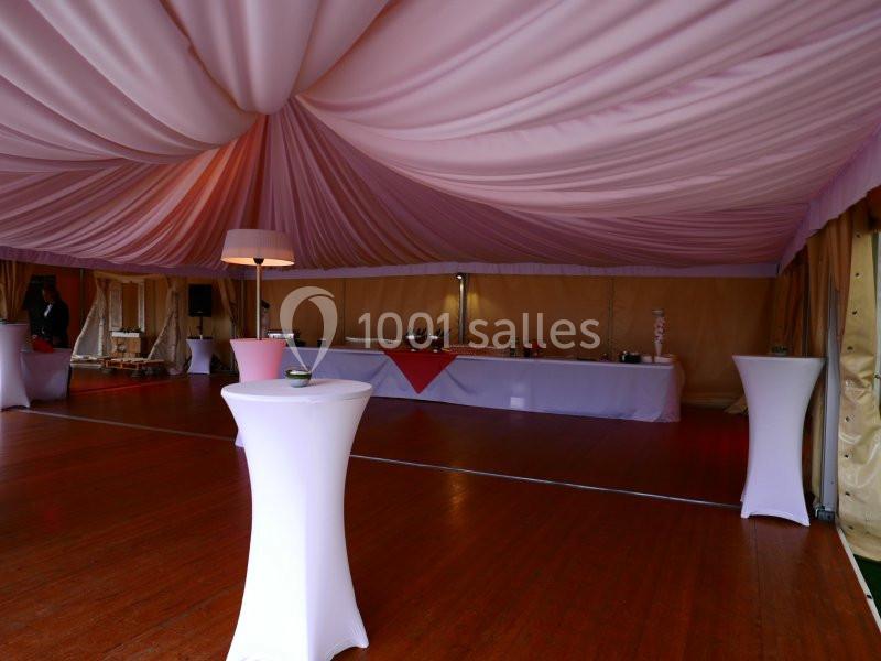 Intérieur d'une tente de réception avec plafond drapé, tables hautes blanches et buffet en arrière-plan.