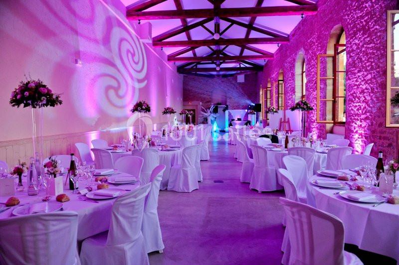 Salle de réception décorée avec des tables rondes dressées, éclairage rose et ambiance festive.