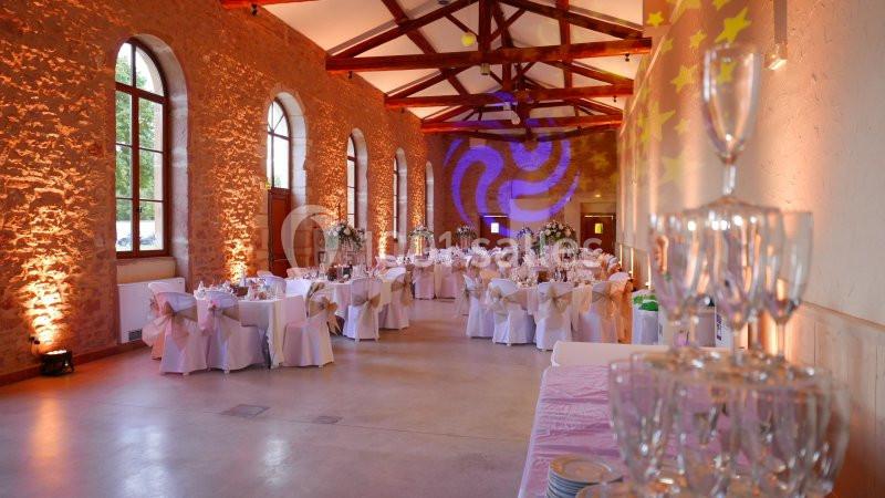 Salle de réception décorée avec des tables dressées, des chaises ornées de nœuds et un éclairage chaleureux.