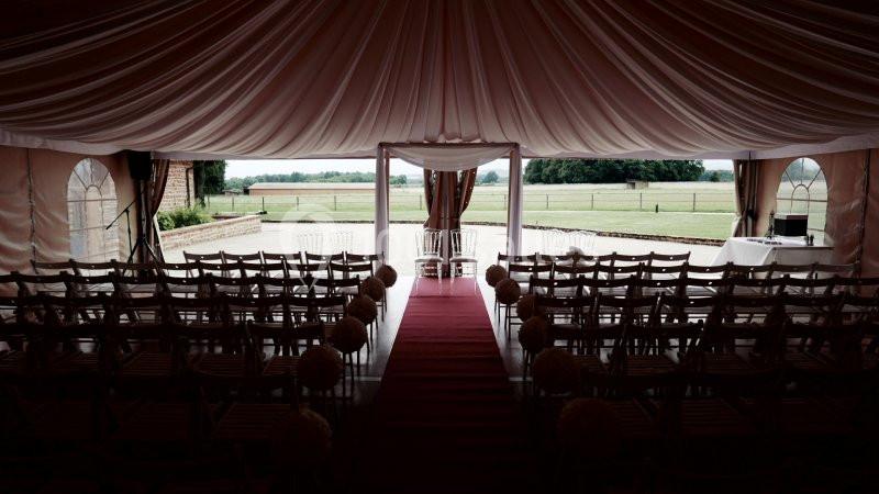 Intérieur d'une tente de réception avec des rangées de chaises alignées et une vue sur un espace extérieur verdoyant.