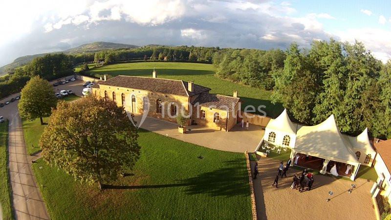 Vue aérienne d'un bâtiment en pierre entouré de verdure avec une tente blanche et des personnes rassemblées à proximité.