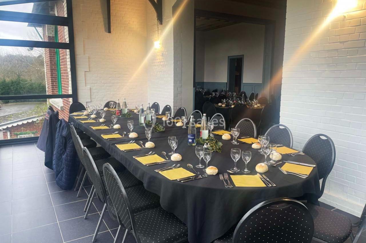 Table dressée avec nappes noires, serviettes jaunes, verres et pains, dans une salle lumineuse avec murs blancs et grandes…