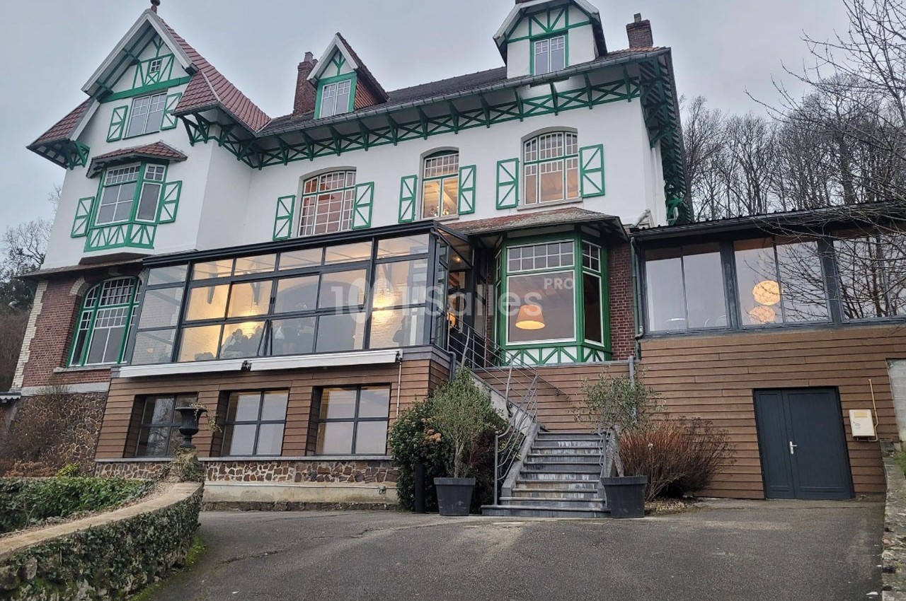 Grande maison à colombages avec façade blanche et verte, baies vitrées modernes et escalier menant à l'entrée principale.