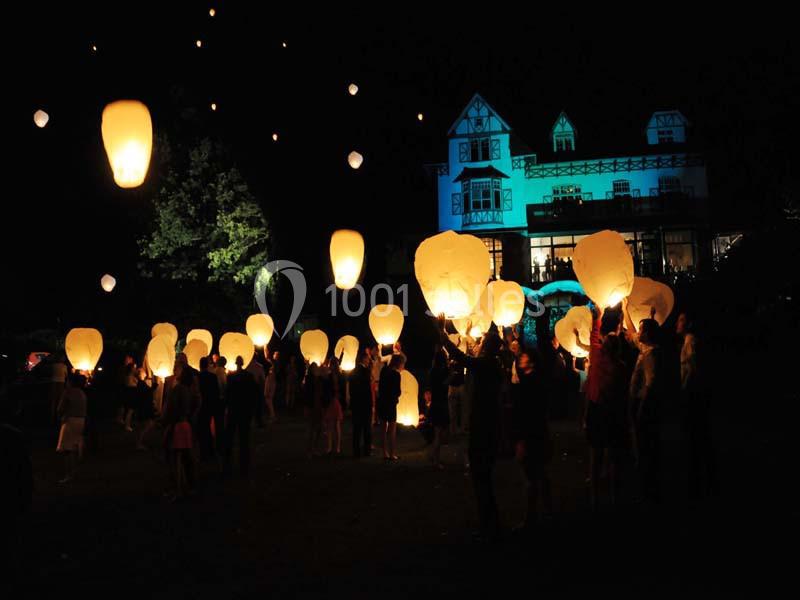 Des personnes libèrent des lanternes lumineuses dans le ciel nocturne devant un bâtiment éclairé.