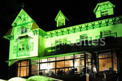 Miniature Location salle Cassel (Nord) - La Grande Maison Réception #20 Grande maison à colombages éclairée en vert la nuit, avec des fenêtres illuminées et un porche couvert.