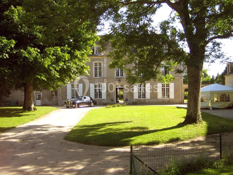 Façade d'un manoir entouré d'arbres, avec une pelouse, une allée et une voiture stationnée devant.