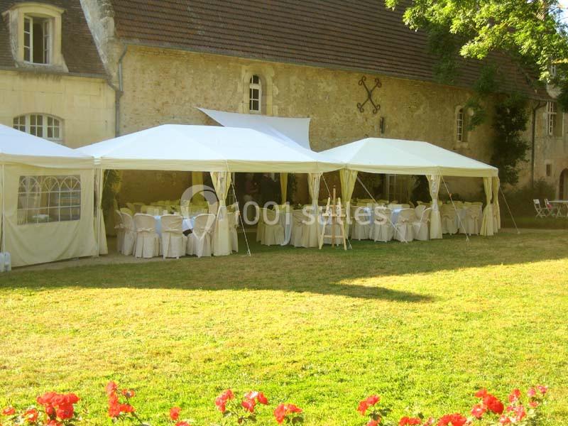 Tentes blanches installées dans un jardin devant un bâtiment en pierre, avec des tables dressées pour un événement.