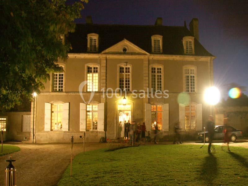 Façade d'un bâtiment ancien éclairé de nuit, avec des fenêtres lumineuses et des personnes à l'entrée.