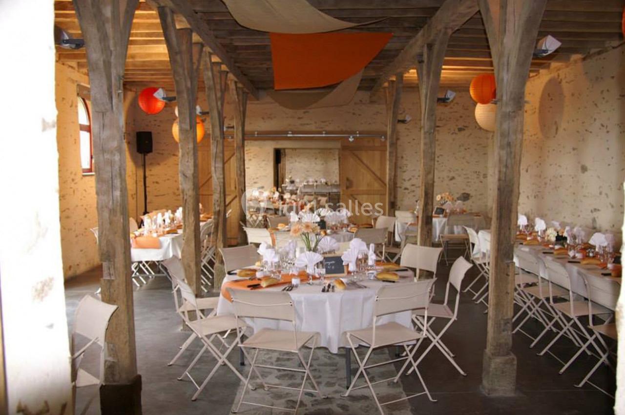 Salle de réception avec tables rondes décorées de nappes blanches, chaises pliantes et lanternes suspendues.