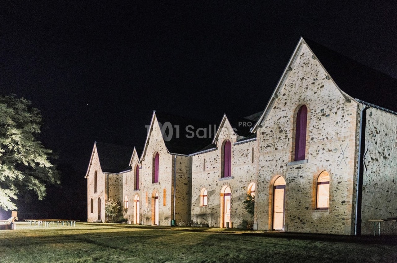 Bâtiment en pierre avec plusieurs façades éclairées et fenêtres en arc, photographié de nuit.