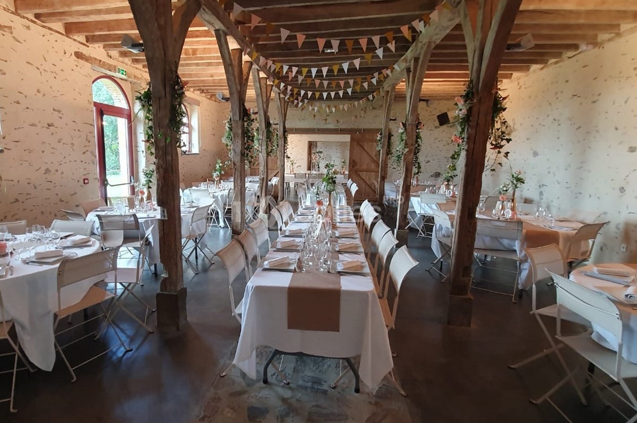 Salle de réception décorée avec des tables dressées, des guirlandes suspendues et des murs en pierre apparente.
