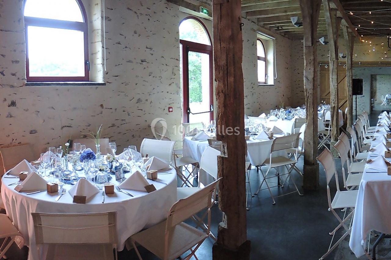 Salle de réception avec tables rondes dressées, nappes blanches, chaises pliantes et décoration florale.