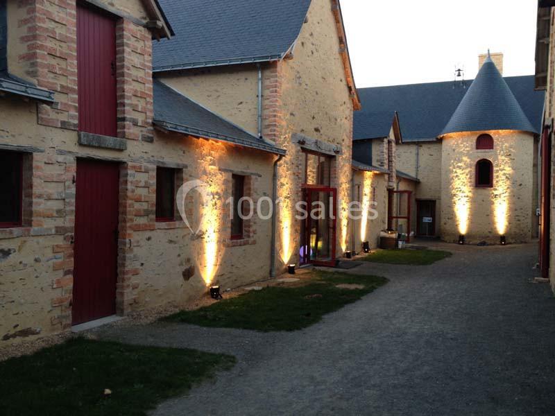 Bâtiments en pierre rénovés avec éclairage extérieur, portes rouges et chemin en gravier au crépuscule.