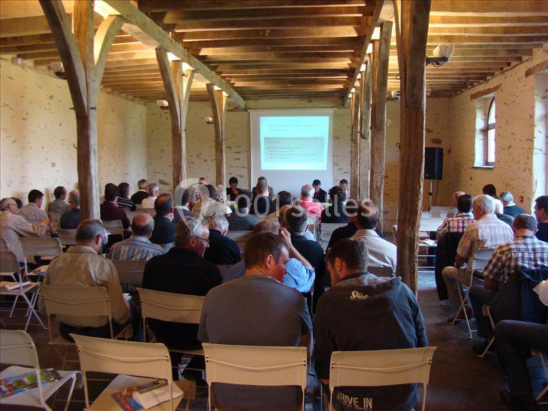 Groupe de personnes assises dans une salle avec poutres apparentes, assistant à une présentation projetée sur un écran.