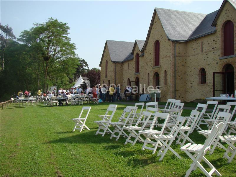 Chaises blanches disposées sur une pelouse devant un bâtiment en pierre, avec des personnes rassemblées au loin.