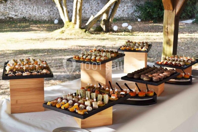 Plateaux de bouchées apéritives variées disposés sur des supports en bois sous un abri extérieur.