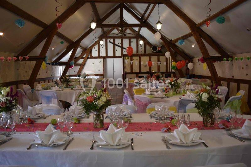 Salle décorée pour un événement avec des tables dressées, nappes blanches, fleurs, ballons et guirlandes colorées.