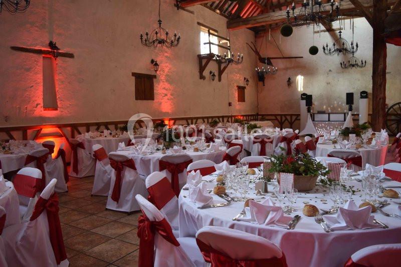 Salle de réception décorée avec des tables rondes, nappes blanches, nœuds rouges et éclairage d'ambiance chaleureux.