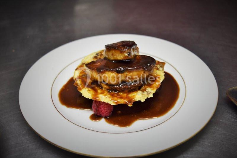 Assiette de foie gras poêlé sur une galette, nappé de sauce brune, avec une framboise en garniture.