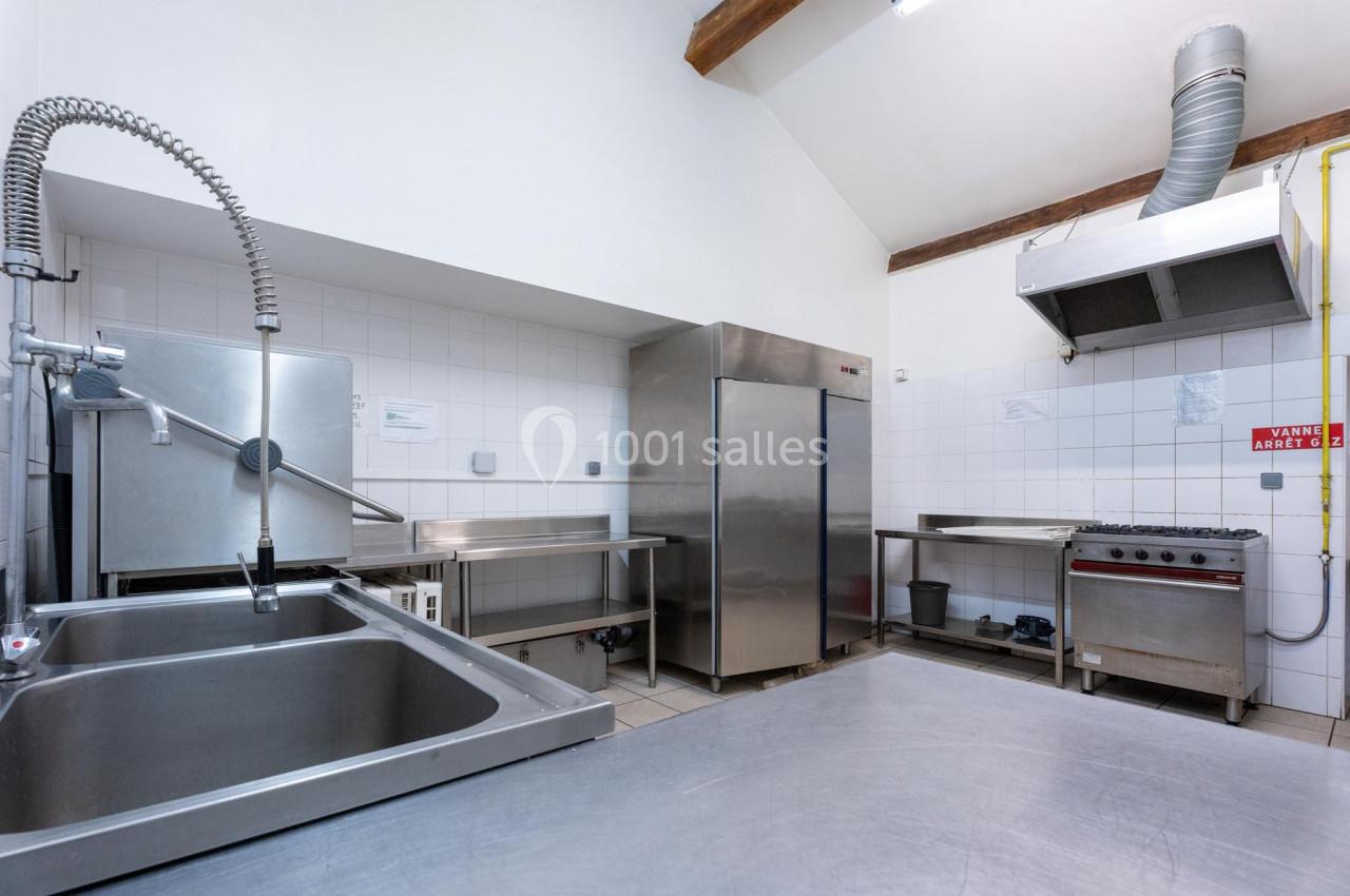 Cuisine professionnelle avec évier inox, réfrigérateur, hotte, plaques de cuisson et plan de travail en acier.