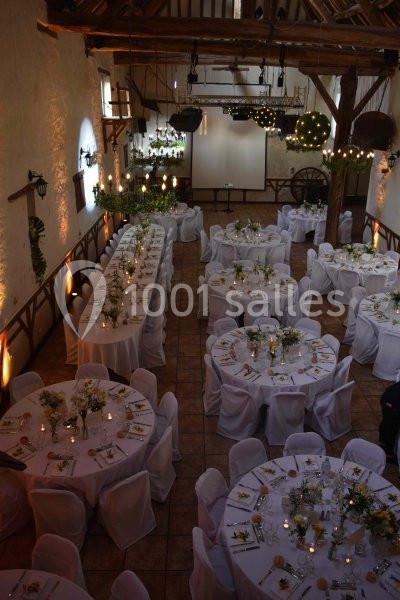 Salle de réception décorée pour un mariage avec des tables rondes et rectangulaires ornées de fleurs et bougies.