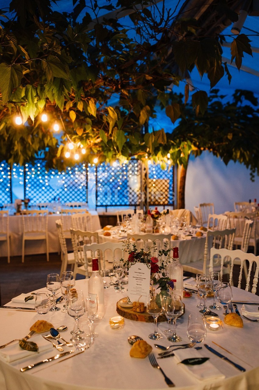 Salle de réception décorée avec des tables dressées, éclairage chaleureux et feuillage suspendu.