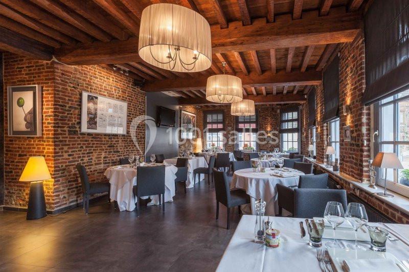 Salle de restaurant élégante avec murs en briques, poutres apparentes, tables dressées et éclairage chaleureux.