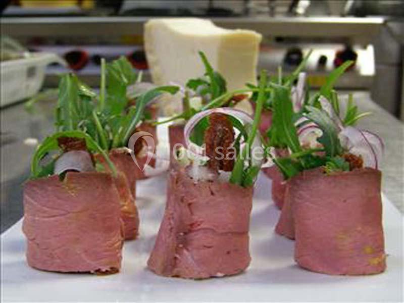 Roulés de viande garnis de roquette, oignons rouges et fromage, disposés sur une assiette blanche en cuisine.